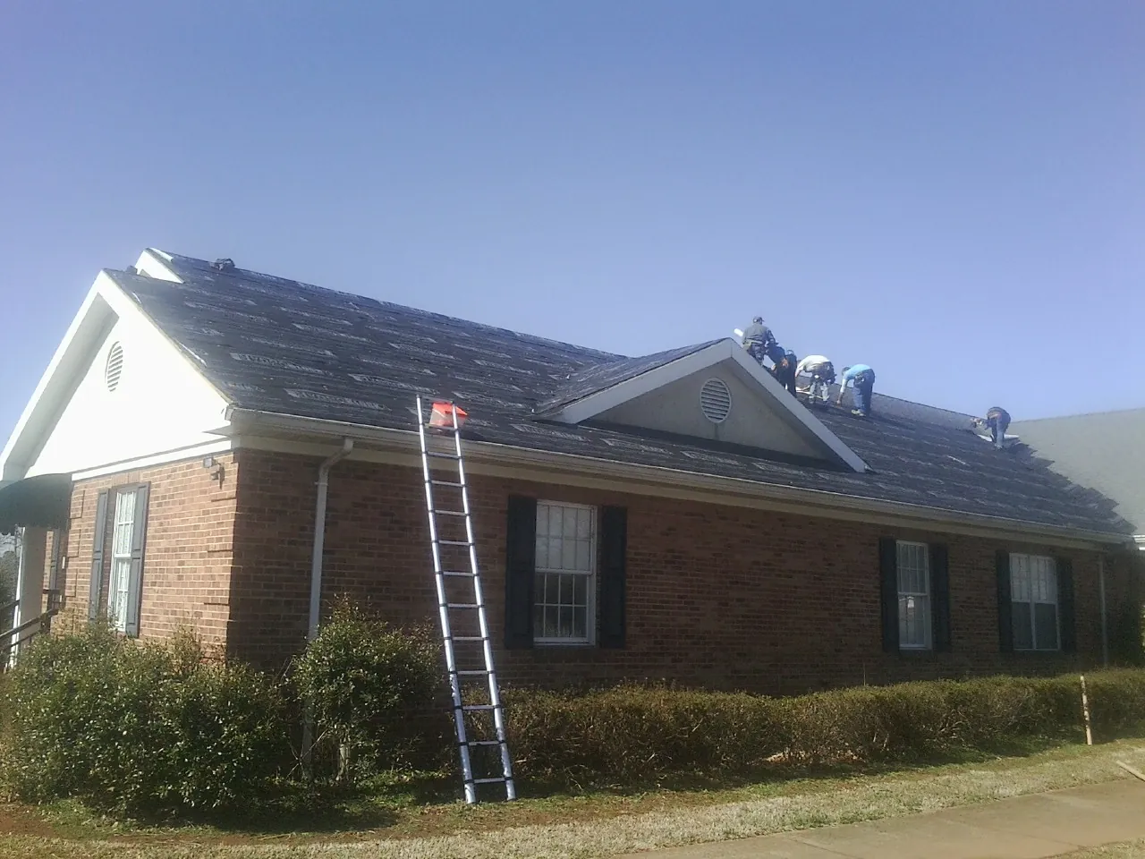 Crew tearing shingles off a brick ranch roof with a ladder set — Metal Roof Repair work by our crew in Hurlock
